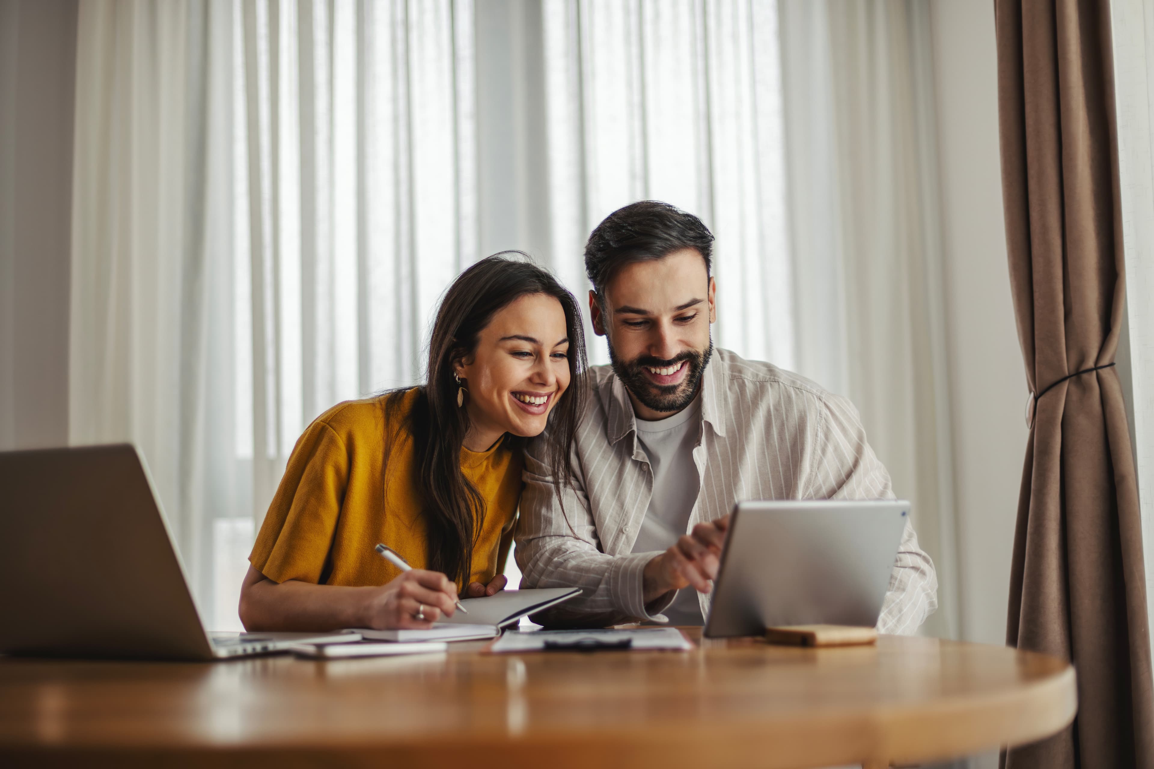 A couple reviewing financial information together using a tablet and notebook.